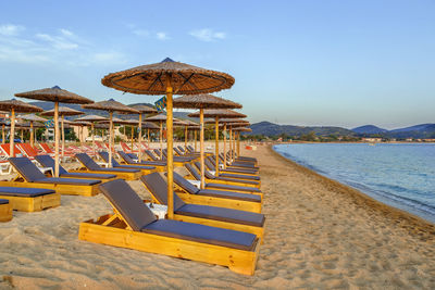 Deck chairs on sand at beach against sky