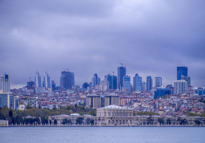 Cityscape at waterfront against cloudy sky