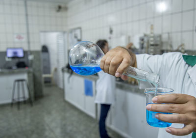 Midsection of scientist pouring liquid in beaker at laboratory