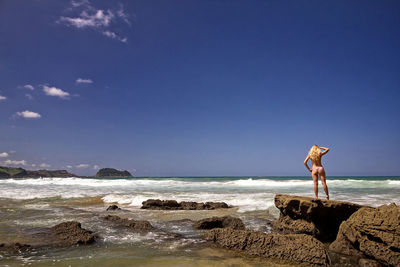 Man standing on rock at beach against blue sky