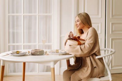 A beautiful blonde young woman in a knitted sweater celebrates the christmas holiday at home