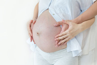 Cropped hands touching stomach of pregnant woman against white background