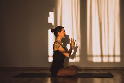 Front view of young sporty woman practicing yoga meditation on black sport mat in a room