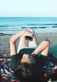 Midsection of young woman at beach against clear sky