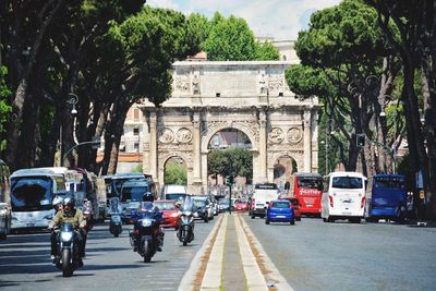 Traffic leading towards arch of constantine amidst trees in city