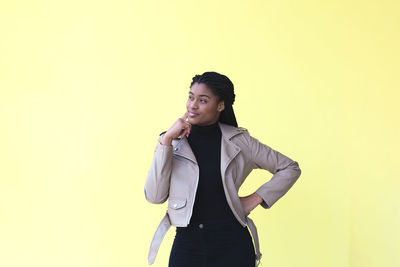 Young woman looking away while standing against yellow background