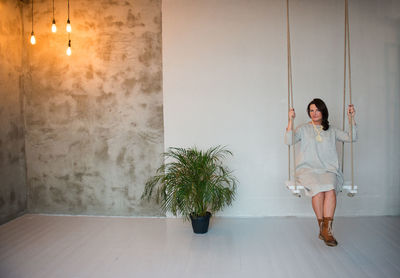 Portrait of woman sitting on swing in illuminated room