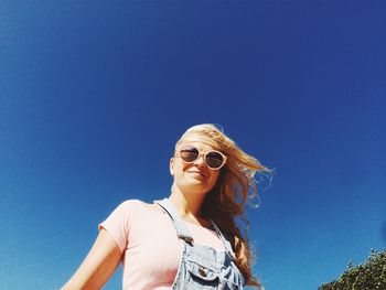 Low angle view of young woman against clear blue sky