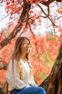 Portraits of young woman  sitting on tree with colorful leaves
