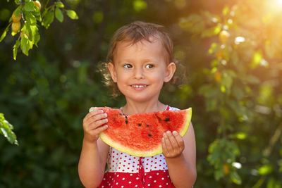 Little curly white girl eating watermelon and smiling on green blurred background
