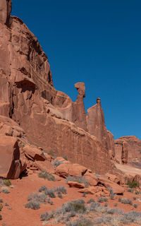 Full frame view of sandstone cliff with rock formations and balancing rock against a clear blue sky
