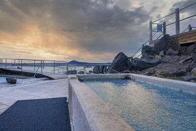 View of pool at natural geothermal spa against cloudy sky during sunset