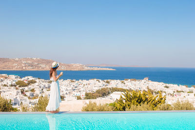 Woman standing by swimming pool against sea