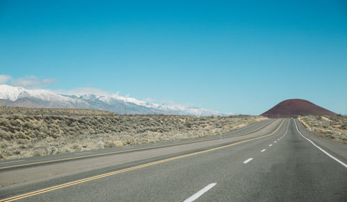 Empty road by mountains against clear sky