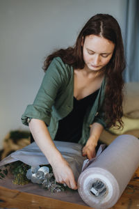 Young woman wrapping decorations on table at home