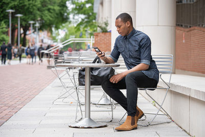 Full length of young man using mobile phone while sitting on seat