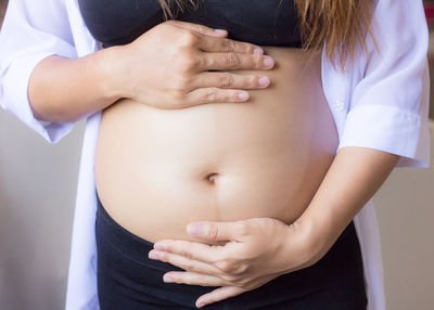 Midsection of pregnant woman making heart shape on stomach 