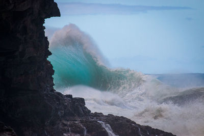 Wave crashing against rocks against sky