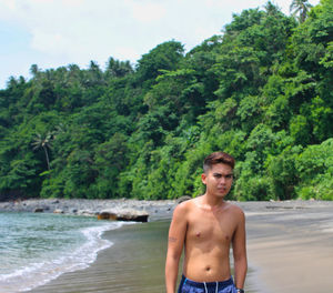 Shirtless young man against trees at beach