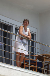 Low angle portrait of smiling woman standing by railing in balcony