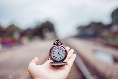 Close-up of person hand holding clock against blurred background