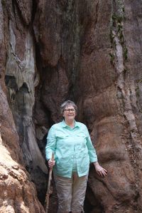 Smiling senior woman standing against sequoia tree trunk