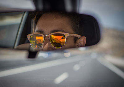 Reflection of man wearing sunglasses on rear-view mirror in car