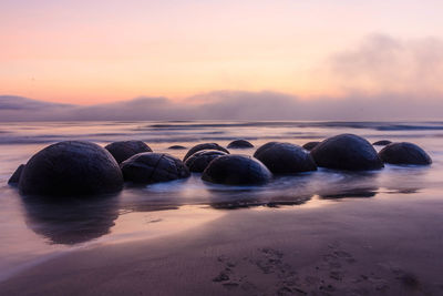 Rocks on beach against sky during sunset