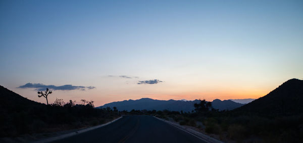 Road by silhouette mountains against sky during sunset