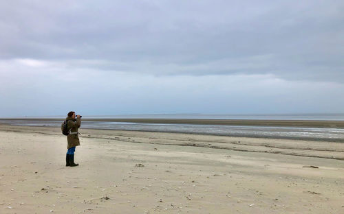 Rear view of woman walking at beach against sky