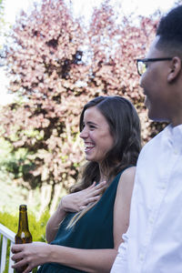 Woman laughing, drinking a bottle of beer during a summer dinner in a garden