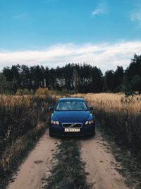 Car on road amidst field against sky