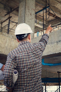 Rear view of man holding coffee while standing at construction site