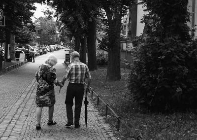 Full length rear view of senior couple holding hands while walking on footpath