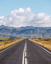 Empty road leading towards mountains against sky