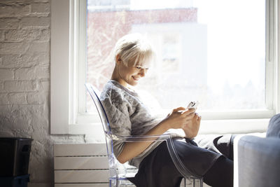 Side view of happy woman using smart phone at home
