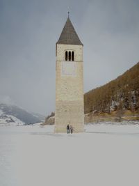 Friends standing on snow covered field by church against sky