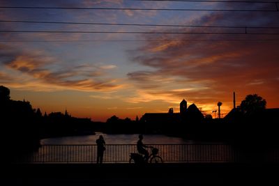 Silhouette people by river against sky during sunset