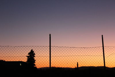 Silhouette fence on field against clear sky during sunset