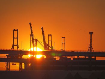 Silhouette cranes at construction site against sky during sunset