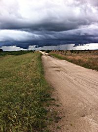 Road passing through field against cloudy sky