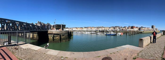 Panoramic view of buildings by river against clear blue sky
