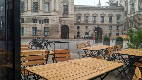 Empty chairs and tables at sidewalk cafe against buildings in city