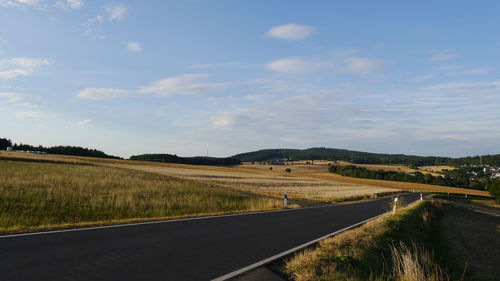 Empty road amidst field against sky with golden light