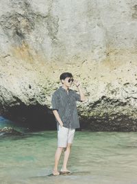 Full length of young man standing on rock by sea