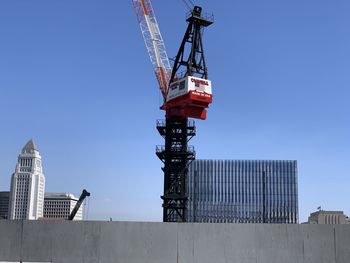 Low angle view of crane by building against clear blue sky