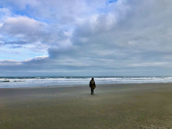 Rear view of woman walking at beach against sky