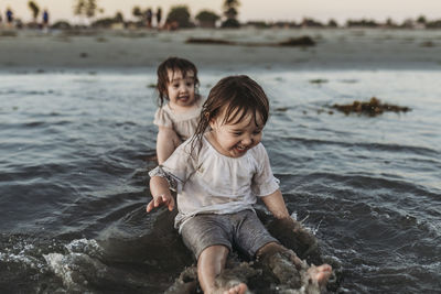 Front view of toddler sisters sitting and splashing in water at beach