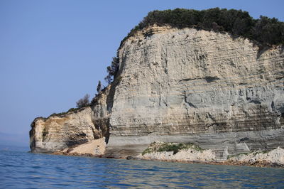 Rock formations by sea against clear sky