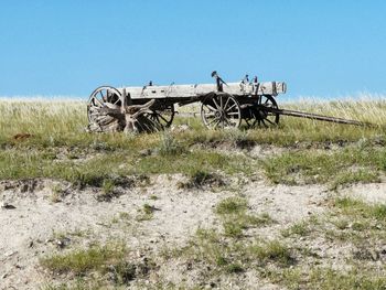 Old push cart on field against clear sky